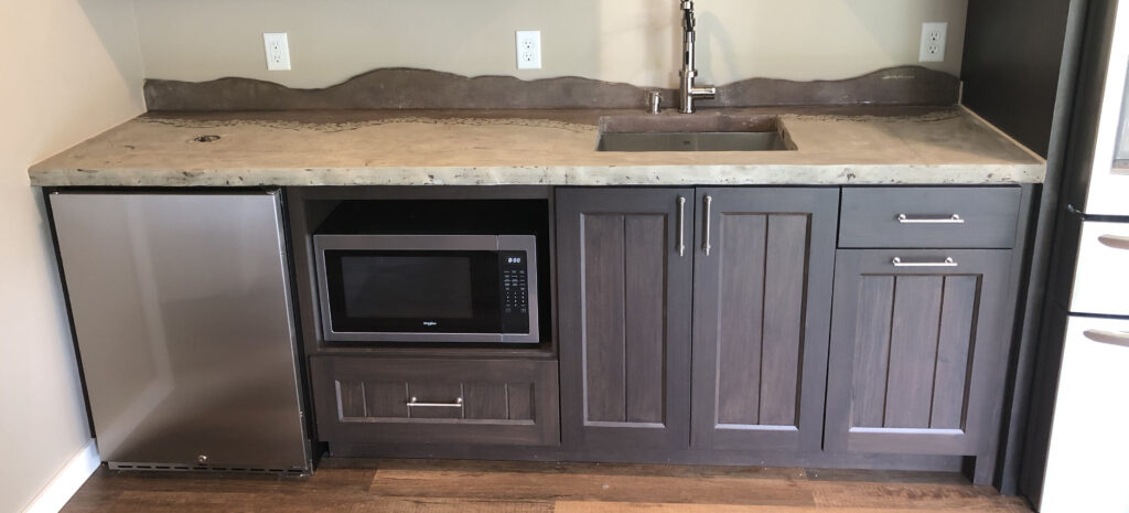 Brown and tan concrete countertops in a basement bar with a concrete mountainous looking backsplash
